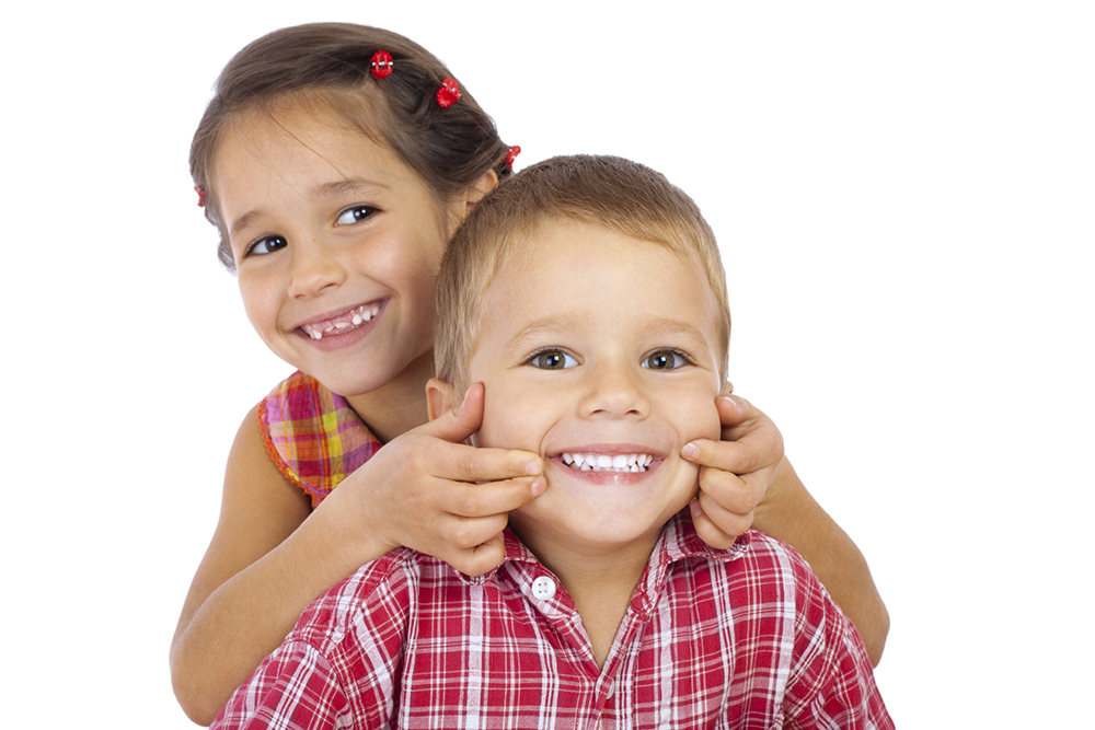 Two funny smiling little children, showing their teeth, isolated on white